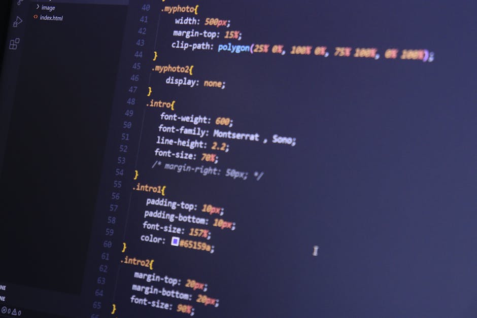 A close-up view of a laptop computer displaying lines of colorful code on a dark background, situated on a wooden desk. Next to the laptop, there is a ceramic coffee mug with a beige background and bl